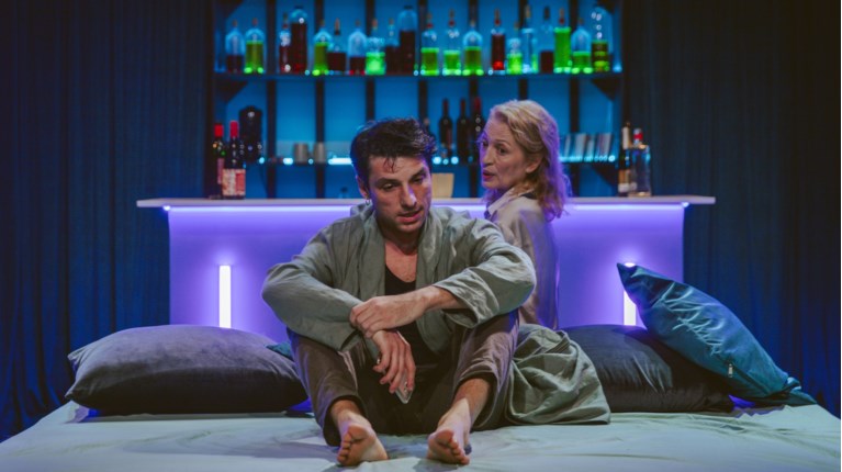 Ο Σπύρος Χατζηαγγελάκης στην παράσταση 'Blue Train'. Μια δυνατή θεατρική σκηνή γεμάτη ένταση και συναίσθημα, με ατμοσφαιρικό φωτισμό και μυστηριώδες σκηνικό.